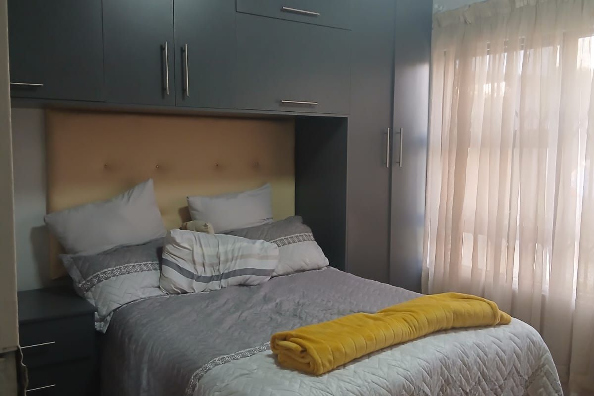 A well-maintained bedroom featuring extensive built-in cabinetry, warm laminate flooring, and a classic tongue and groove ceiling finish.