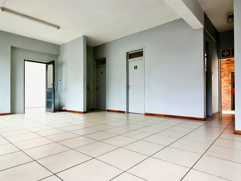 An open-plan industrial office space featuring neutral painted walls, tiled flooring, and multiple internal access doors.