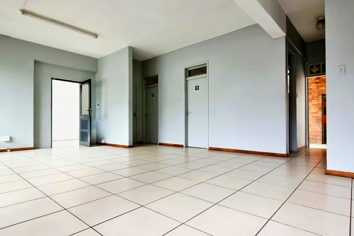 An open-plan industrial office space featuring neutral painted walls, tiled flooring, and multiple internal access doors.