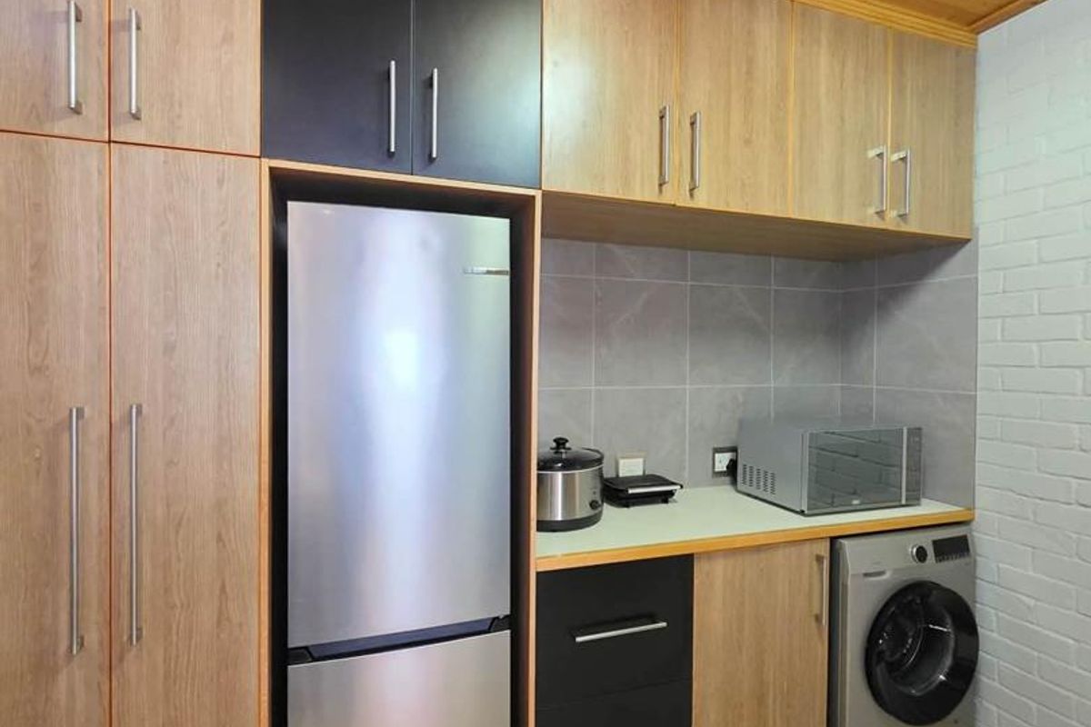 A functional laundry area featuring modern two-tone cabinetry, tiled backsplash, and a timber-paneled ceiling, providing efficient storage and utility space.