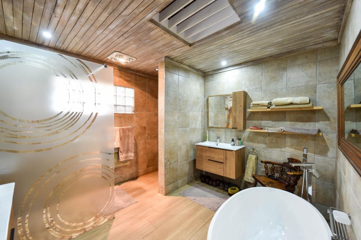 Modern bathroom featuring a freestanding bathtub, vanity with basin, frosted glass shower screen, and unique timber ceiling with a skylight.