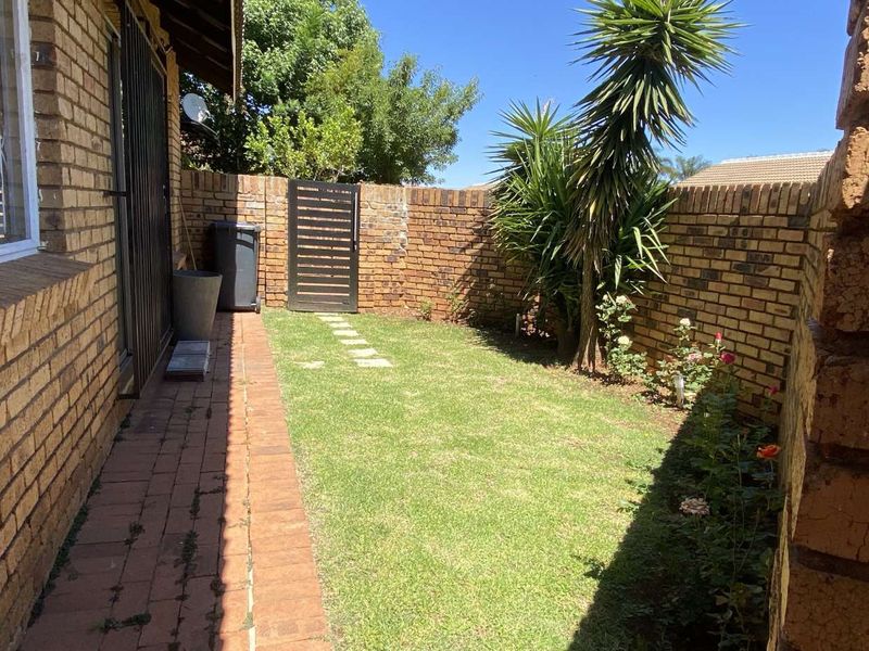 A private rear garden area featuring a brick boundary wall, paved walkway, and a secure metal pedestrian gate.
