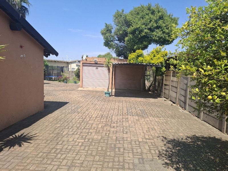 Rear exterior view featuring a paved driveway, double garage, and a carport, enclosed by a precast concrete boundary wall.
