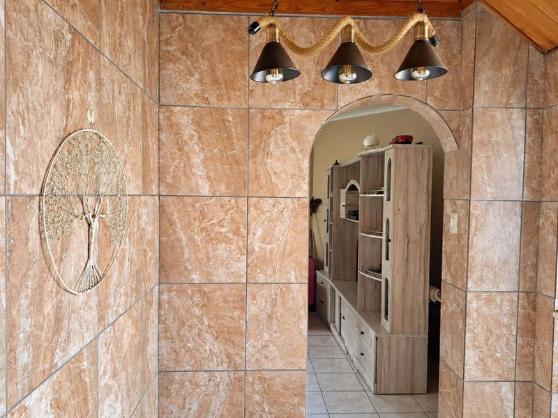 A hallway featuring floor-to-ceiling marble-effect wall tiles, an arched entryway, and a rustic rope-style pendant light fixture.