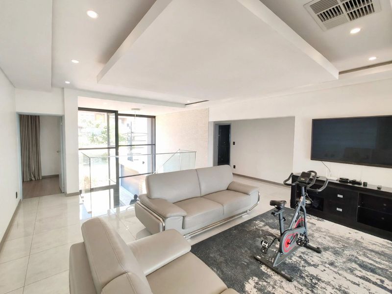 Spacious modern living area featuring a recessed ceiling with downlights, tiled flooring, and a glass balustrade overlooking the lower level.