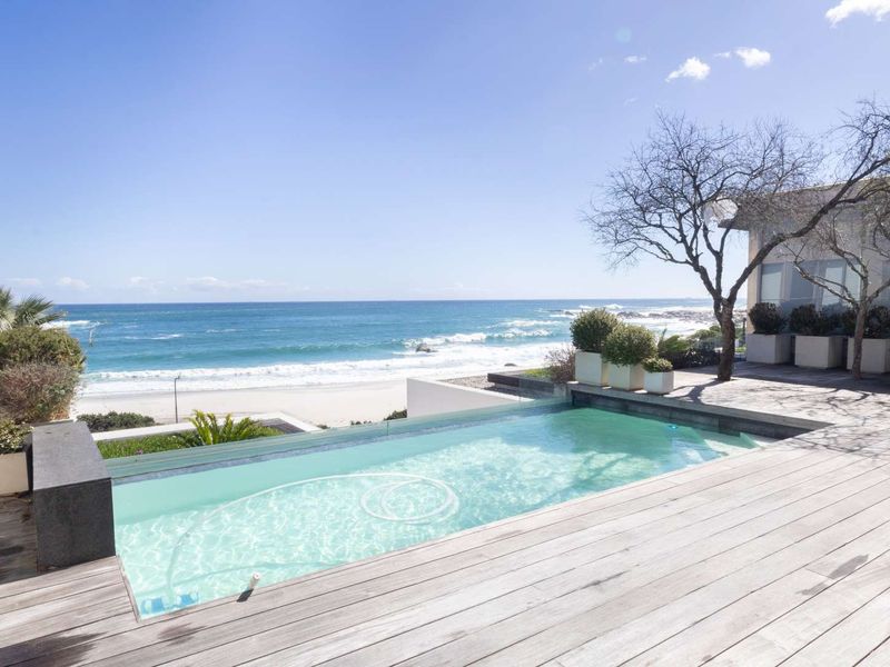 A stunning outdoor pool area featuring timber decking and a glass balustrade, offering direct views of the ocean and beach.