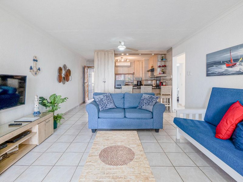 Open-plan living area featuring tiled floors, a ceiling fan, and a functional kitchen with built-in cabinetry and a breakfast counter.