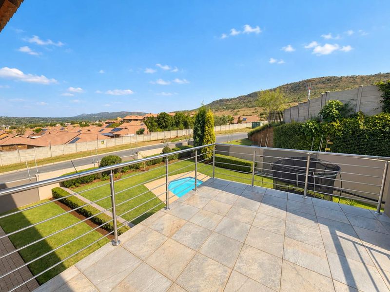 Elevated balcony with stainless steel balustrade overlooking a private garden, swimming pool, and surrounding residential estate.