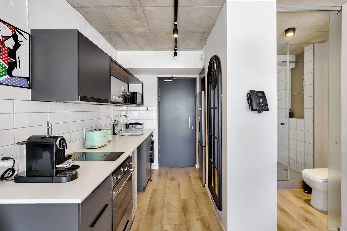 Modern kitchen featuring sleek dark cabinetry, subway tile backsplash, and exposed concrete ceilings, seamlessly transitioning into a contemporary bathroom area.