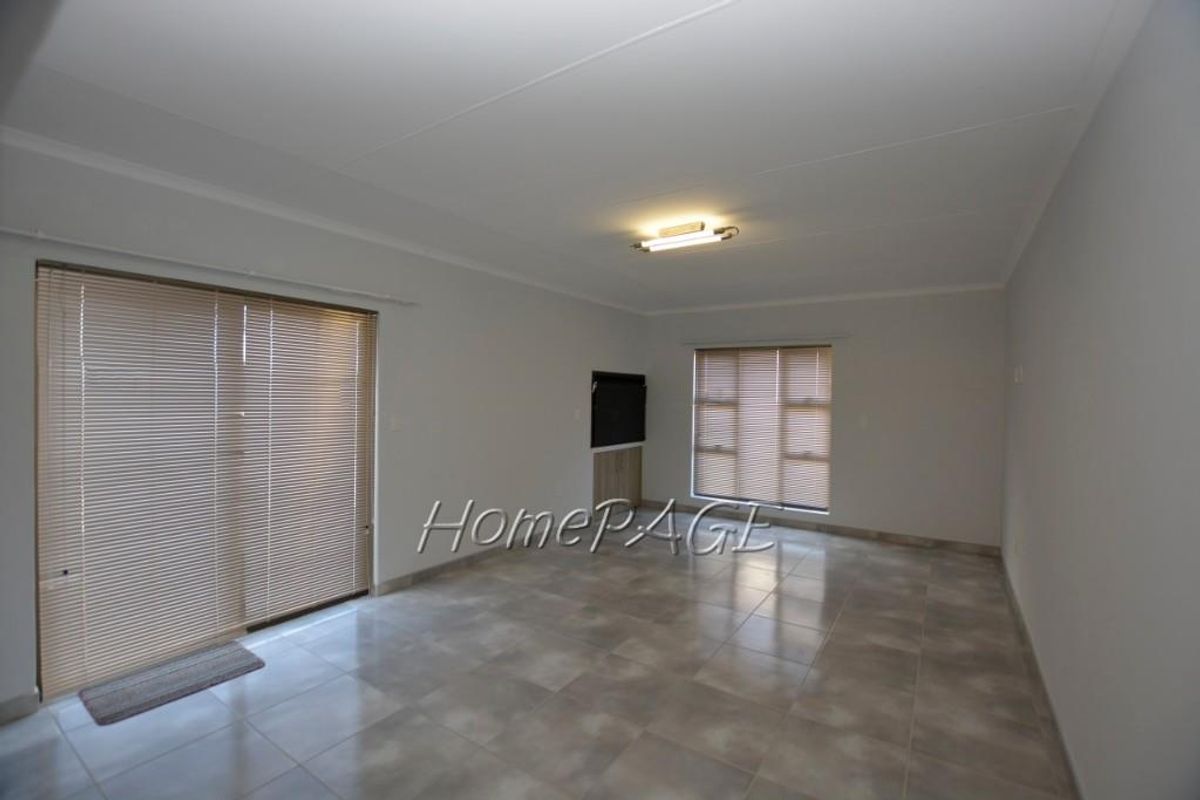 A spacious, neutral living area featuring tiled flooring, large sliding glass doors with blinds, and a built-in media cabinet.