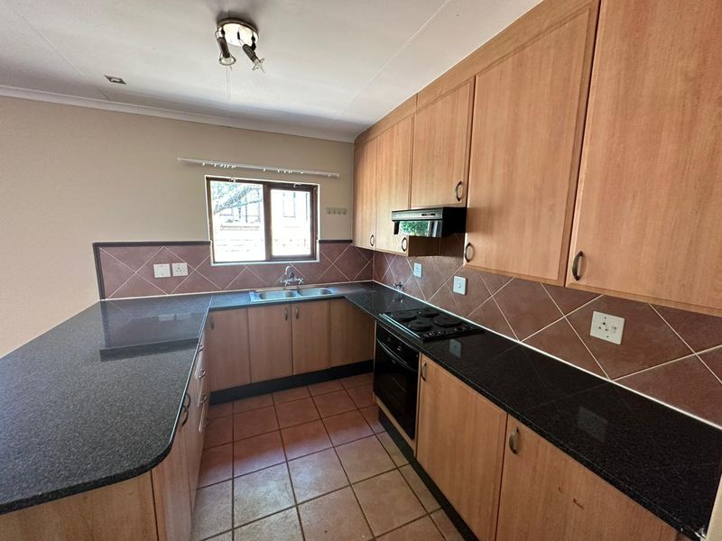 A functional kitchen featuring laminate cabinetry, granite countertops, built-in oven, electric hob, and tiled flooring, offering a clean and practical workspace.