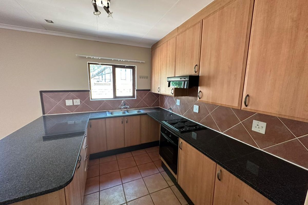 A functional kitchen featuring laminate cabinetry, granite countertops, built-in oven, electric hob, and tiled flooring, offering a clean and practical workspace.