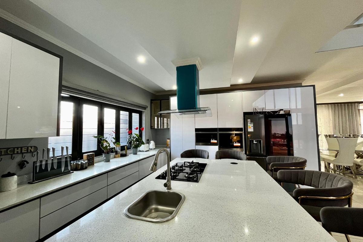 Modern kitchen featuring a large central island with a built-in gas hob, stainless steel sink, and sleek high-gloss cabinetry with integrated appliances.