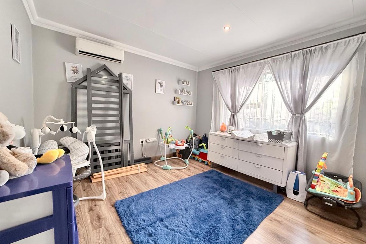 A well-maintained bedroom featuring laminate flooring, a wall-mounted air conditioning unit, and security bars on the window.