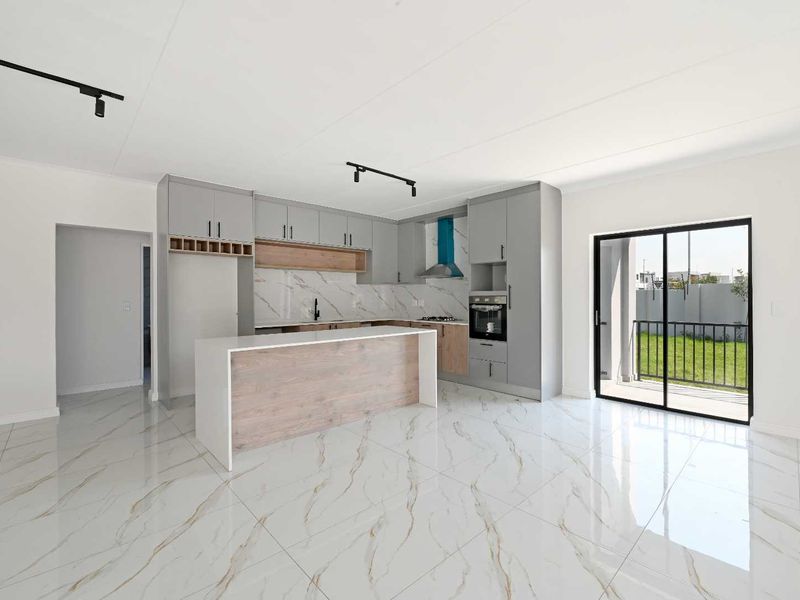 Modern open-plan kitchen featuring sleek cabinetry, a central island, built-in oven, and high-gloss marble-look floor tiles, leading to an outdoor patio area.