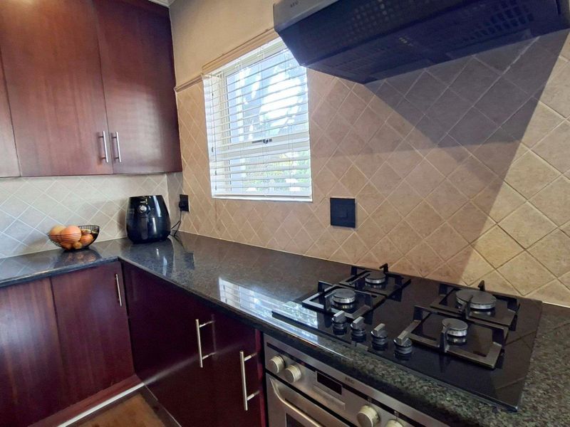A functional kitchen featuring dark wood cabinetry, granite countertops, a gas hob, built-in oven, and a tiled backsplash.