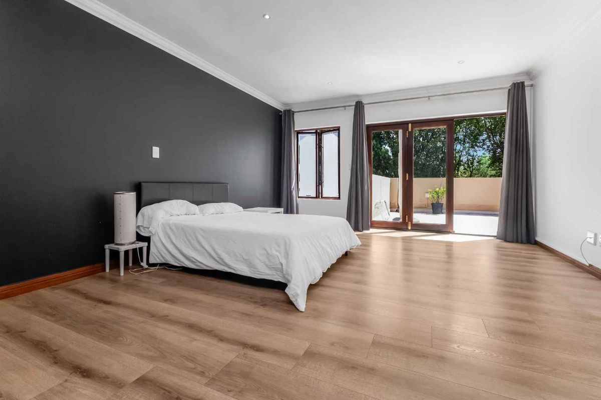 Spacious bedroom featuring modern laminate flooring, a dark accent wall, and double glass doors providing direct access to an outdoor patio area.