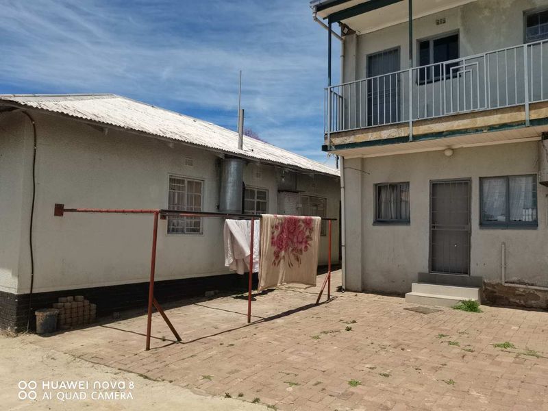 Rear courtyard area featuring paved flooring, a two-story building section with a balcony, and a single-story structure with a corrugated metal roof.