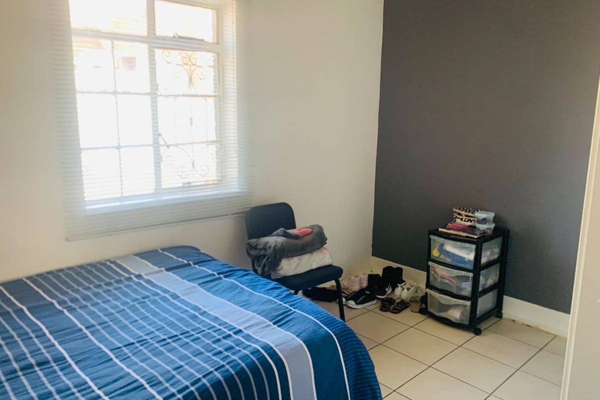 A bedroom featuring tiled flooring, a window with security bars, and a dark accent wall.