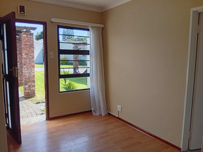 An empty living room featuring laminate flooring, a louvre window, and direct access to the exterior patio area.