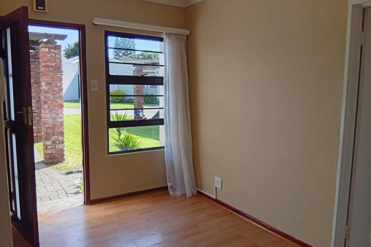 An empty living room featuring laminate flooring, a louvre window, and direct access to the exterior patio area.