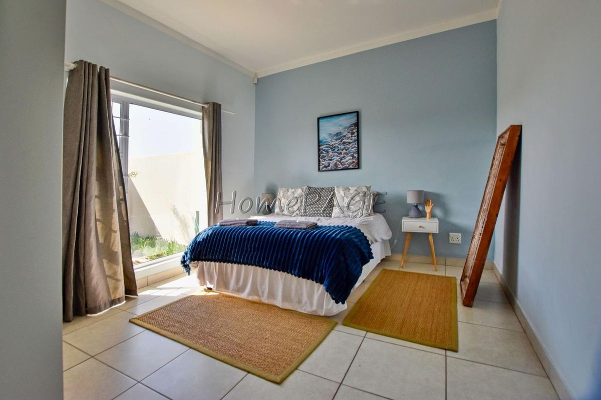 A well-lit bedroom featuring tiled flooring, neutral wall paint, and a large window providing natural light and access to the exterior.