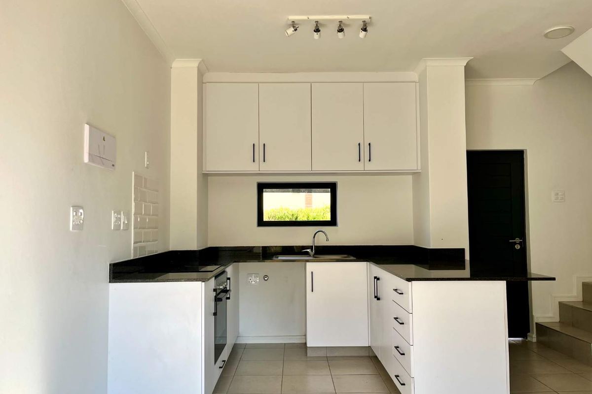 A clean, modern kitchen featuring white cabinetry, dark granite countertops, built-in oven, and tiled flooring in an open-plan layout.