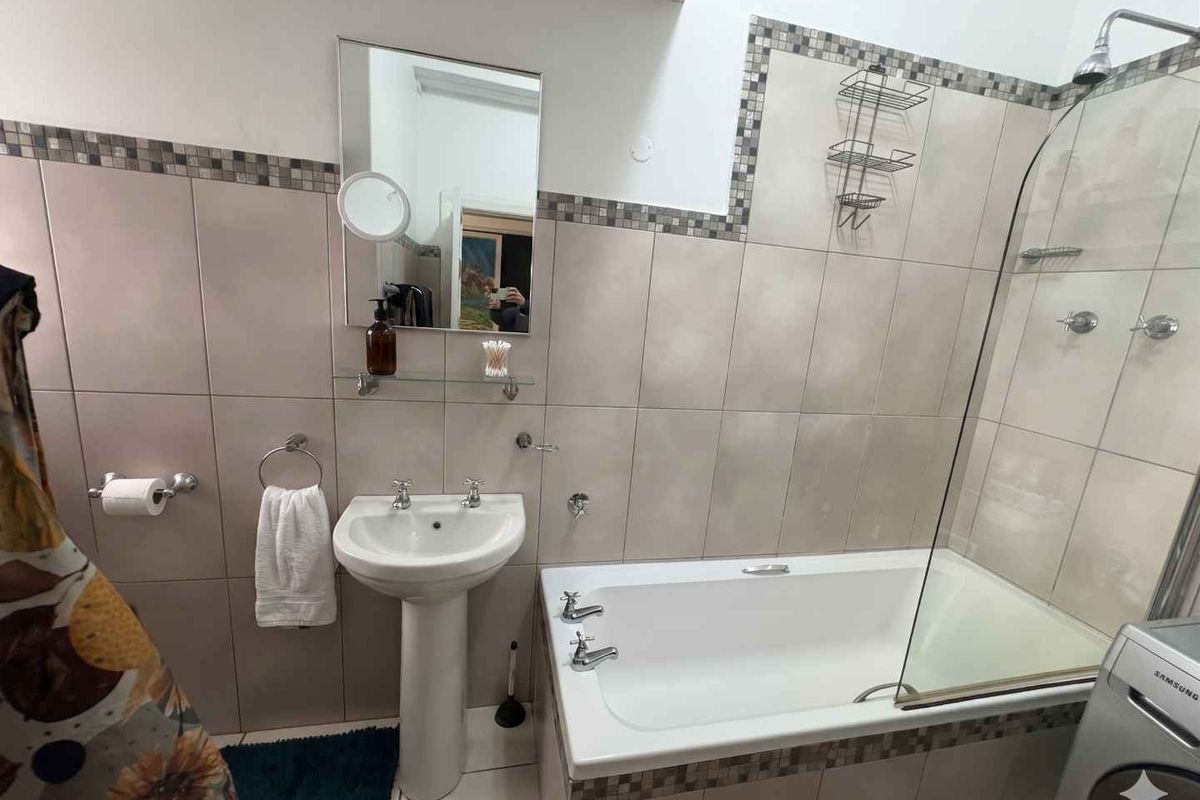 A functional bathroom featuring a pedestal sink, a bathtub with a glass shower screen, and tiled walls with decorative mosaic accents.