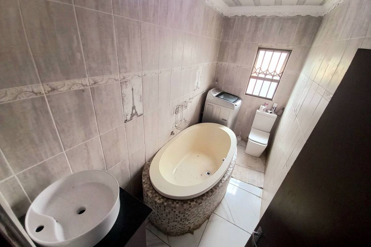A compact bathroom featuring a built-in oval bathtub, a modern vessel sink, and a standard toilet with tiled walls and flooring.