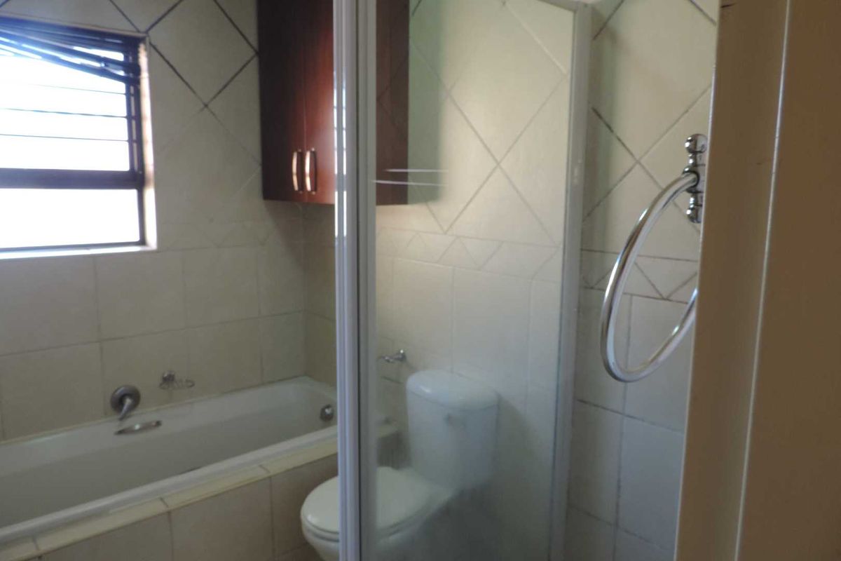 A dated bathroom featuring a bathtub, separate shower enclosure, toilet, and wall-mounted storage cabinet with tiled finishes throughout.