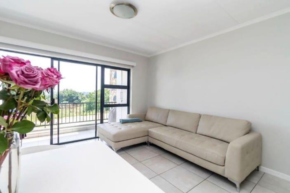A bright living room featuring neutral tiled flooring and a large sliding glass door that provides access to an outdoor balcony area.