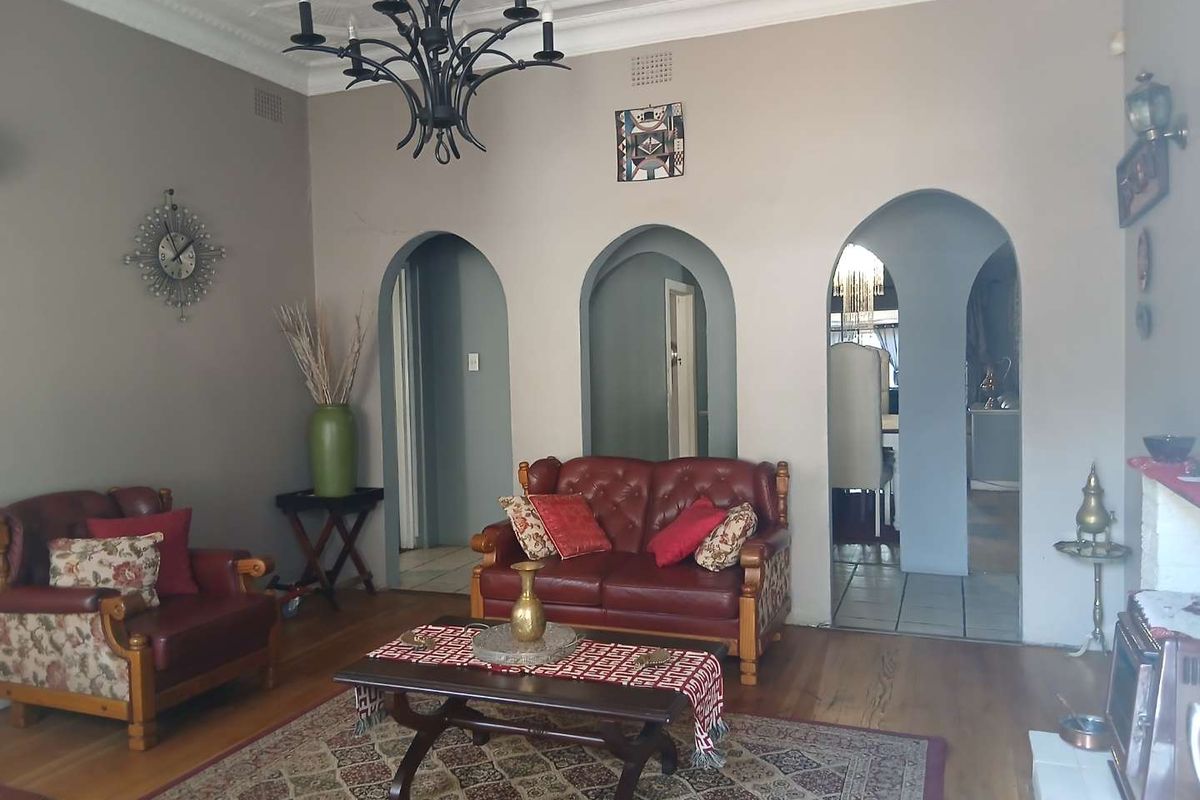 Spacious living room featuring classic hardwood flooring, distinctive arched doorways, and an ornate ceiling cornice, providing a character-filled foundation for modern updates.