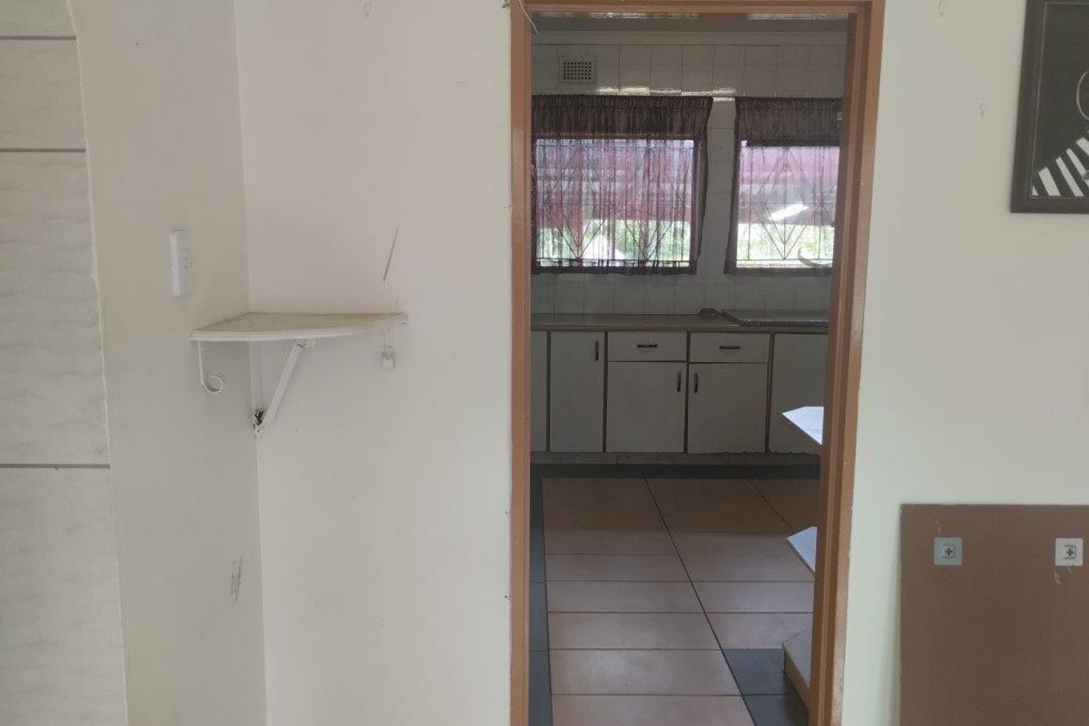 A view through a doorway into a dated kitchen featuring built-in cabinetry, tiled flooring, and a tiled splashback.