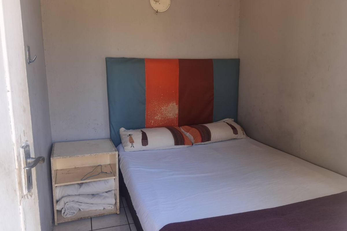 A compact bedroom featuring tiled flooring and a simple layout, currently requiring cosmetic updates to the wall finishes and lighting.