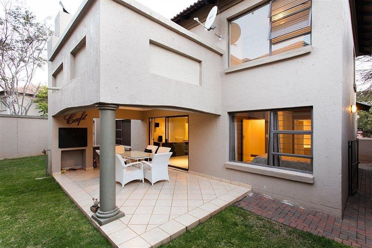 Rear view of the townhouse featuring a covered patio area with built-in braai, tiled flooring, and access to the garden and interior living spaces.