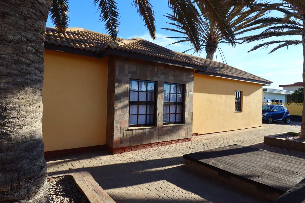 A view of the rear exterior of the house, featuring a paved patio area, stone-clad wall accents, and a tiled roof.
