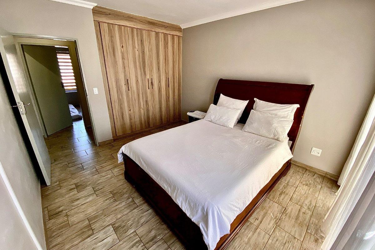 A well-maintained bedroom featuring wood-look tiled flooring, built-in wooden cupboards, and neutral wall finishes.
