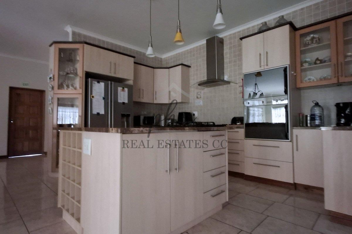 A functional kitchen featuring light-toned cabinetry, a central island, built-in oven, extractor fan, and tiled finishes throughout.