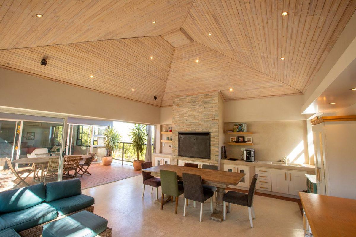 Spacious open-plan living area featuring a vaulted timber ceiling, stone-clad fireplace, and seamless flow to an outdoor patio through large sliding glass doors.