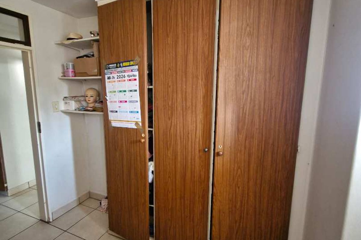 A bedroom featuring built-in wooden wardrobe cabinetry and tiled flooring, providing functional storage space within the apartment.