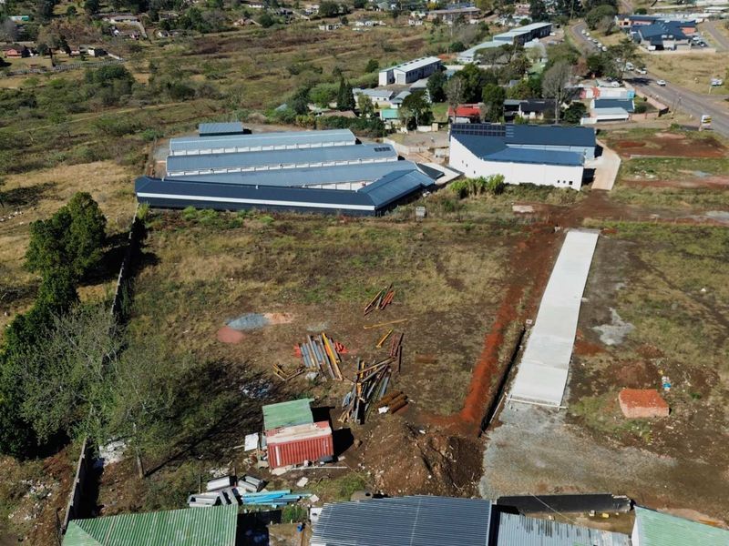 Aerial view of a commercial vacant land plot featuring existing warehouse structures, a concrete driveway, and surrounding perimeter fencing.
