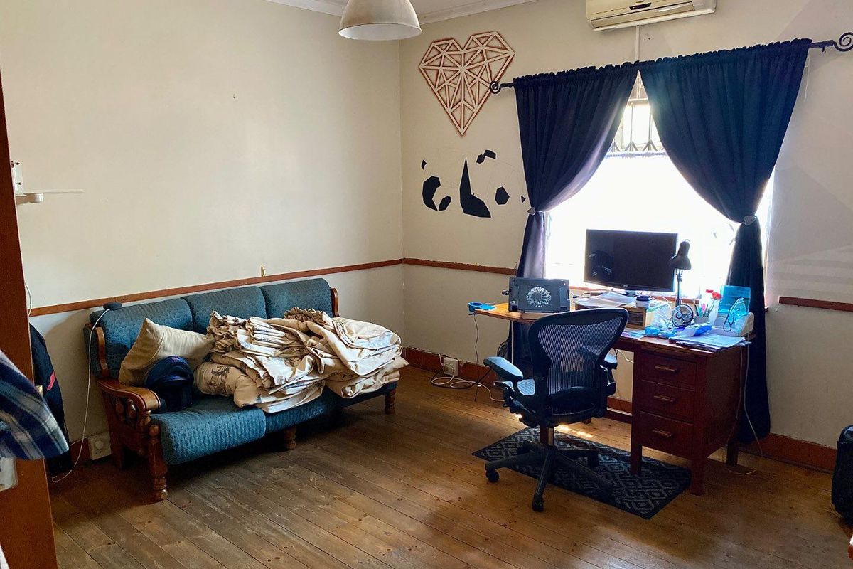 A multi-purpose room featuring original timber flooring, a wall-mounted air conditioning unit, and a window with dark curtains.