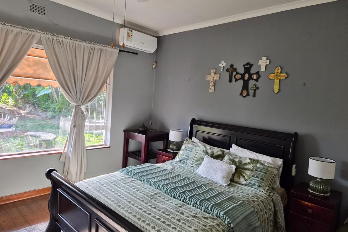 A comfortable bedroom featuring timber flooring, a split-system air conditioner, and large windows overlooking the garden.