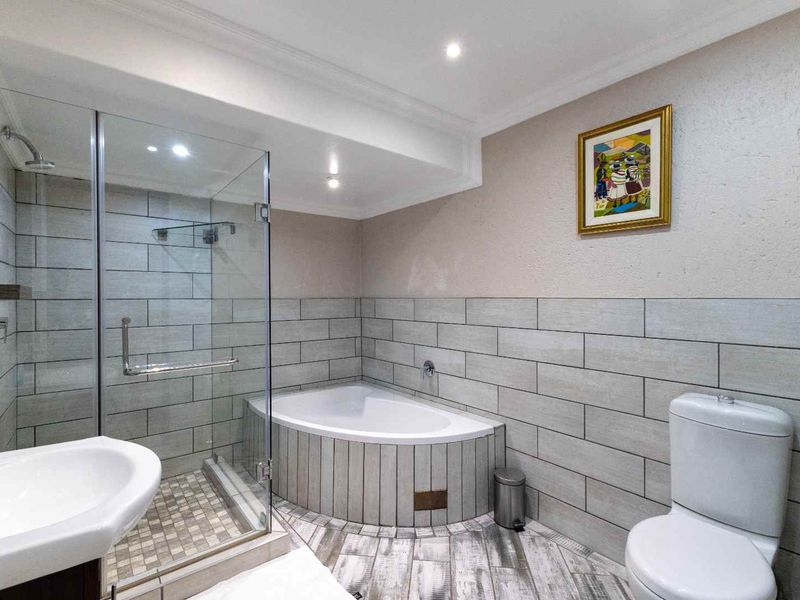 Modern bathroom featuring a glass-enclosed shower, corner bathtub, pedestal basin, and dual-flush toilet with contemporary tiled finishes.