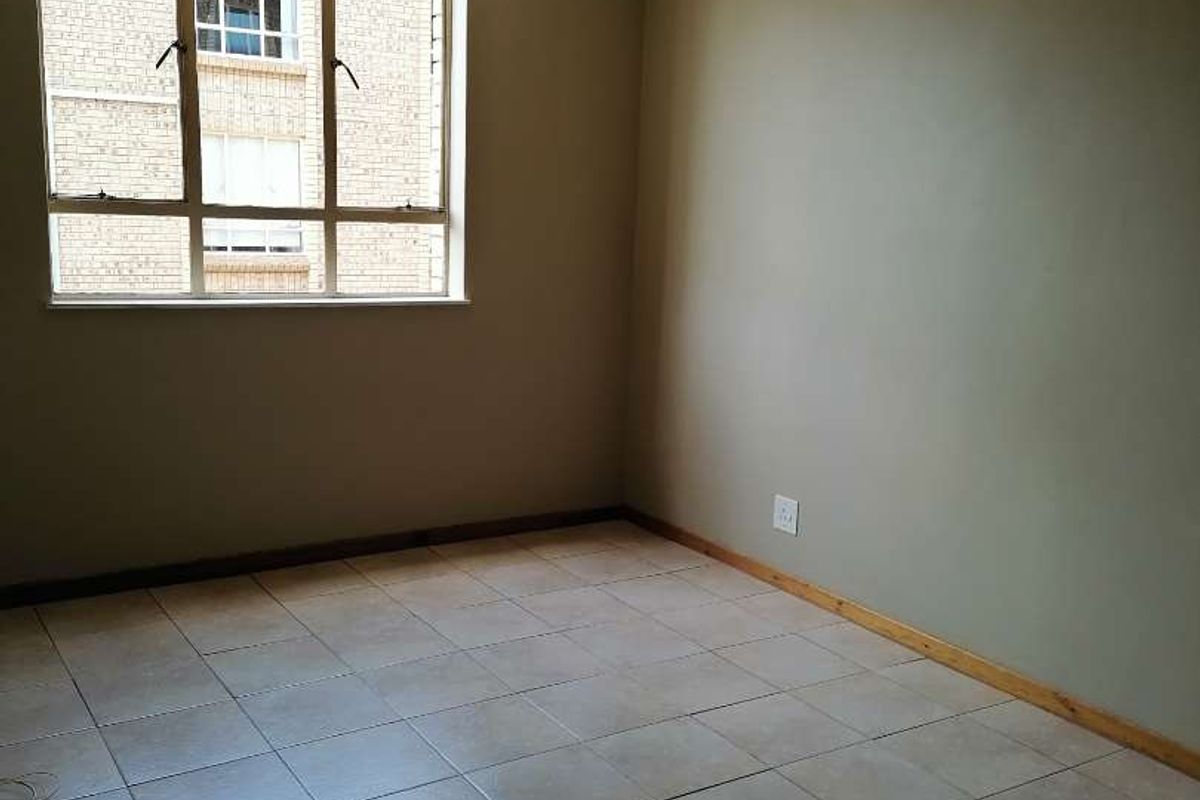 An empty bedroom featuring neutral wall paint, tiled flooring, and a large window providing natural light.