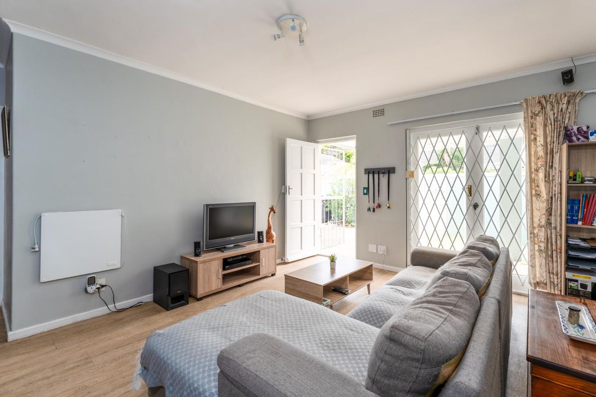 A comfortable living room featuring light wood-look flooring, a ceiling-mounted light fixture, and double doors leading to an outdoor area with security gates.