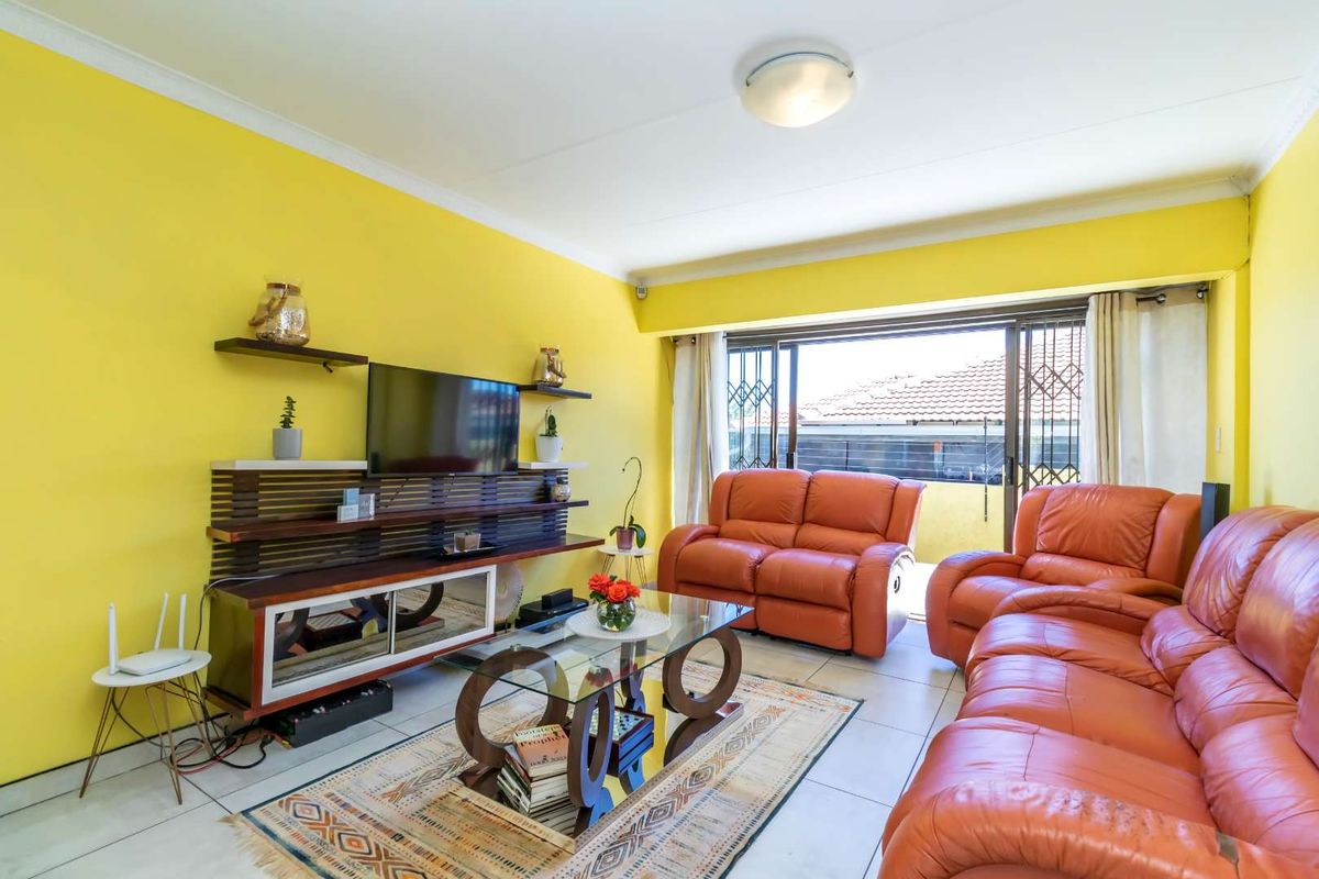 A bright living room featuring tiled flooring, large sliding glass doors with security gates, and access to an outdoor patio area.