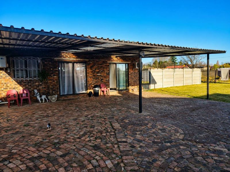 A spacious covered patio area featuring brick paving, exposed brick exterior walls, and sliding glass door access to the main dwelling.