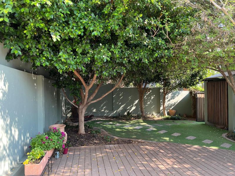 A well-maintained private garden featuring timber decking, artificial lawn, mature trees, and a secure boundary wall with a timber gate.