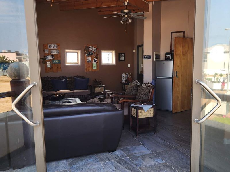A living room featuring exposed timber ceiling beams, a ceiling fan, and tiled flooring, accessible through large sliding glass doors.